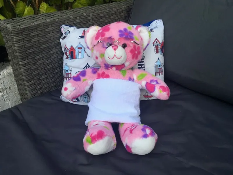 A pink floral bear wrapped in a white towel wearing sunglasses, drying in the sun on an outdoor sofa