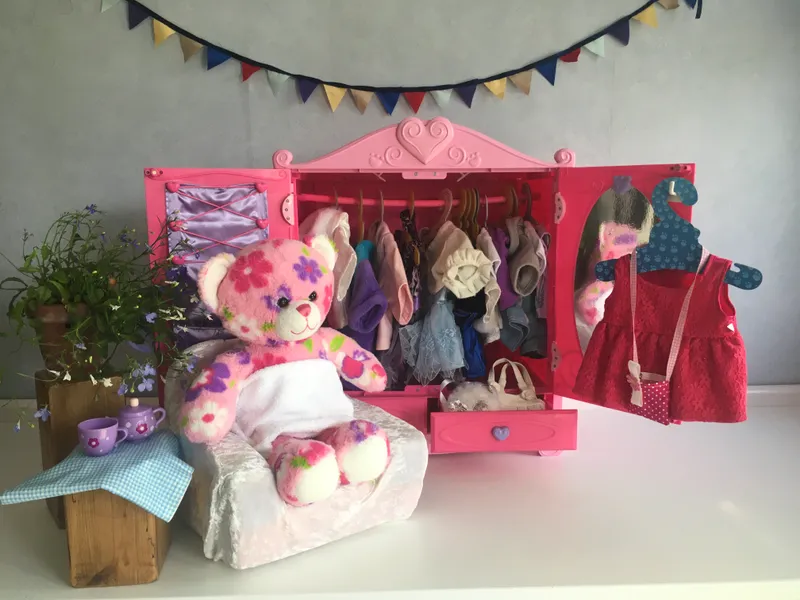 A pink floral bear standing at a pink wardrobe full of tiny outfits, browsing through the clothes