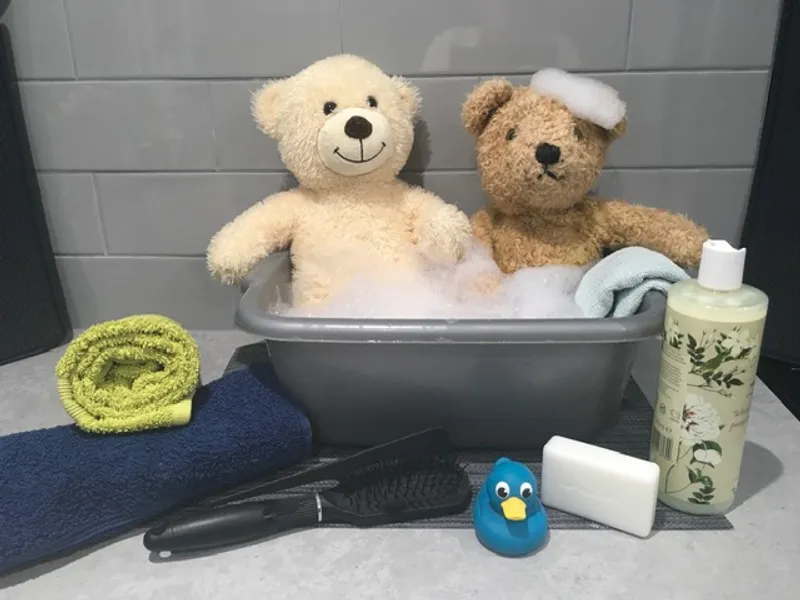 Two bears sitting in a bubble bath with towels, soap, a brush, and a rubber duck